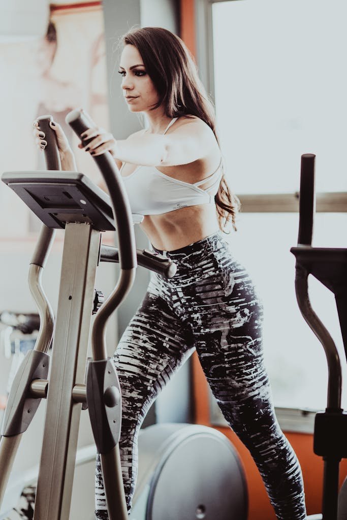 Determined fit sportswoman exercising on modern elliptical cross trainer in light fitness center