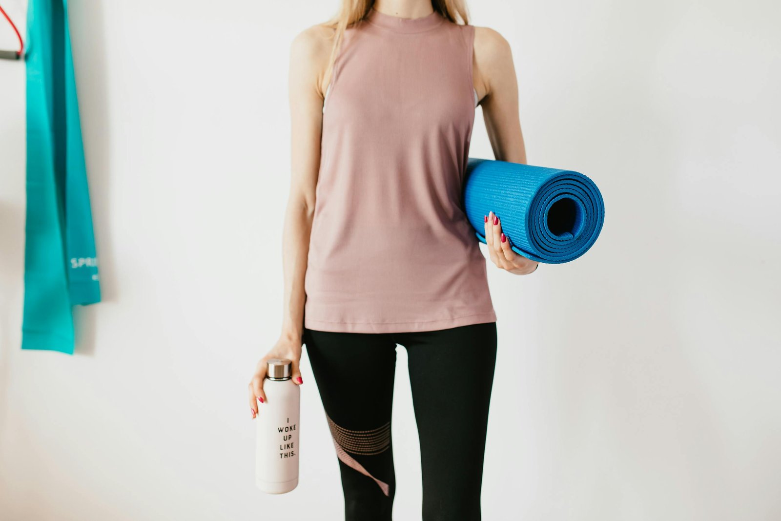 Faceless slim female athlete in sportswear standing with blue fitness mat and water bottle while preparing for indoors workout