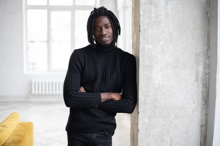 Cheerful black man with dreadlocks leaning on door and looking at camera