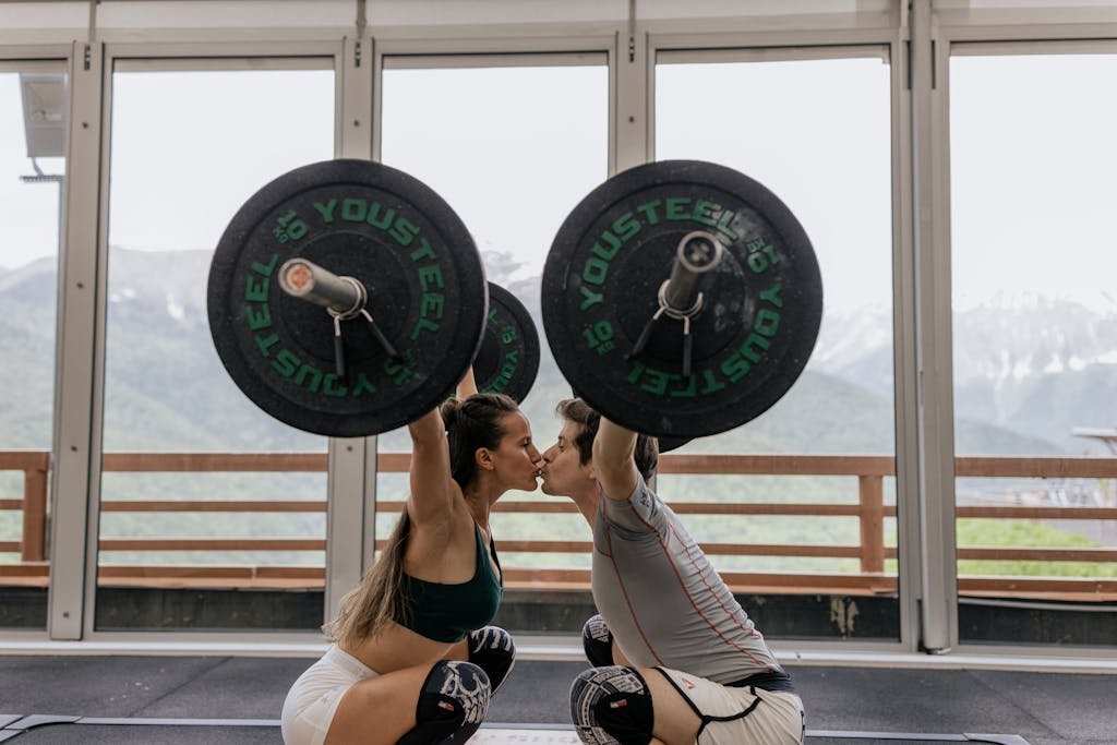 Couple Kissing While Lifting Barbells