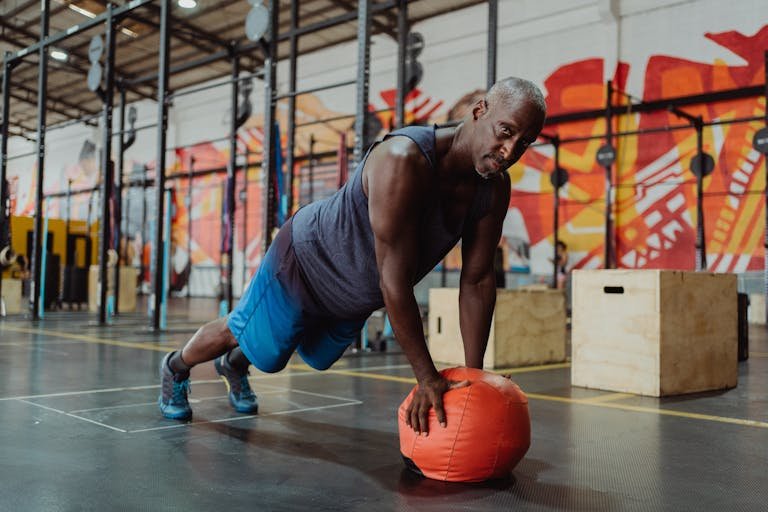 Man in Blue Tank Top and Blue Shorts Doing Push Up Using a Fitness Ball