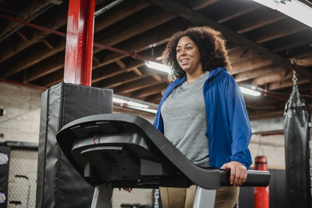 Woman smiling as she exercises on a treadmill, indoor gym environment.